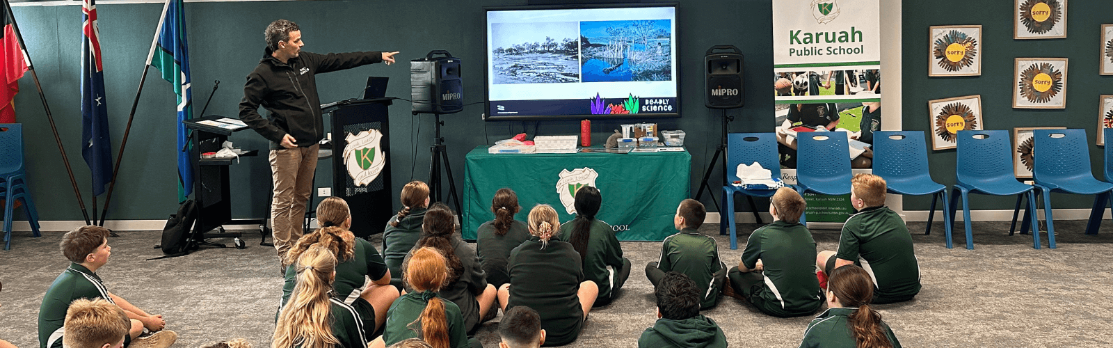 Educator presenting to learners in a classroom setting with a screen displaying images.
