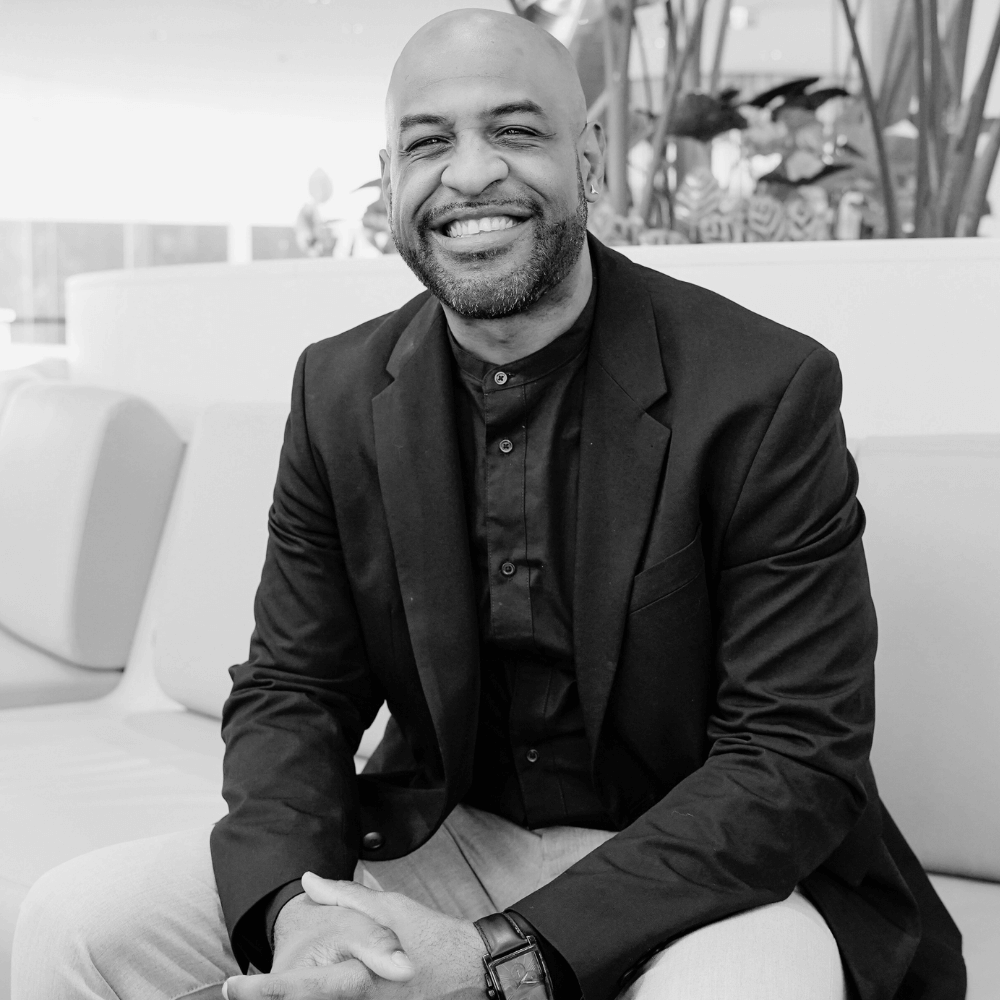 Black and white photo of Board member Henry Cooper sitting on a couch outdoors with a blurred background