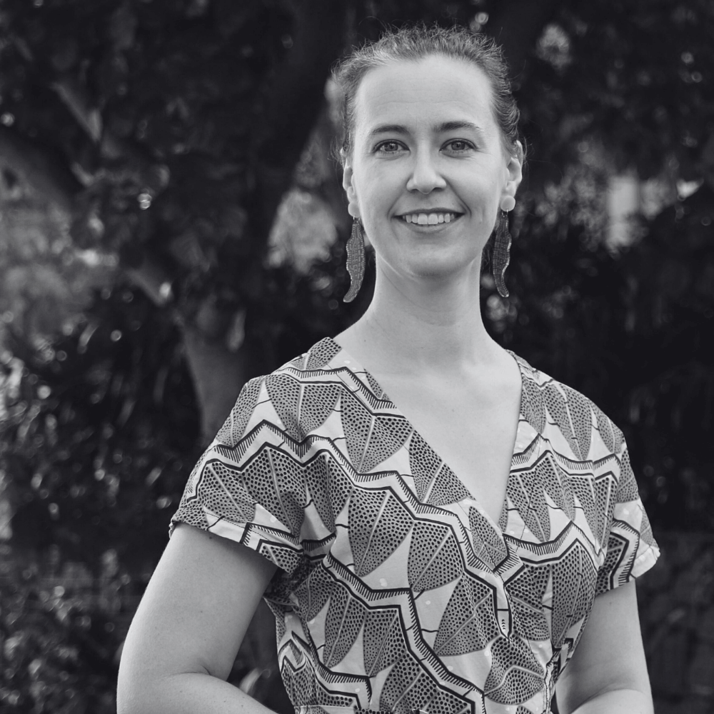 Black and white photo of  Biripi and Worimi woman and Board member Jessica Tapp.  She is wearing a patterned dress with a blurred natural background.